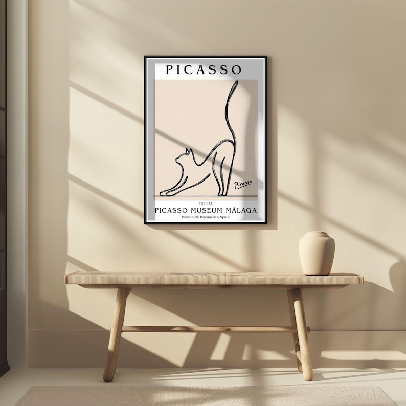 Puede incluir: Un cuadro enmarcado con un dibujo lineal negro de un gato estir&aacute;ndose. El cuadro incluye el nombre "PICASSO" en la parte superior y "PICASSO MUSEUM M&Aacute;LAGA" en la inferior, sobre un fondo beige claro.