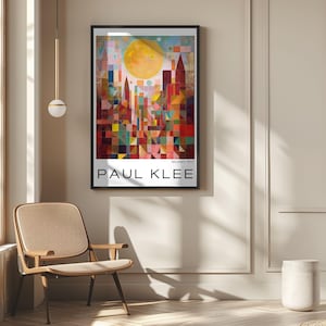 Peut inclure: Une affiche encadr&eacute;e repr&eacute;sentant un paysage urbain abstrait color&eacute; avec un grand soleil jaune. L'affiche est intitul&eacute;e "PAUL KLEE" et "Modern Art". L'&oelig;uvre est expos&eacute;e sur un mur beige, avec une chaise et une suspension luminaire visibles.