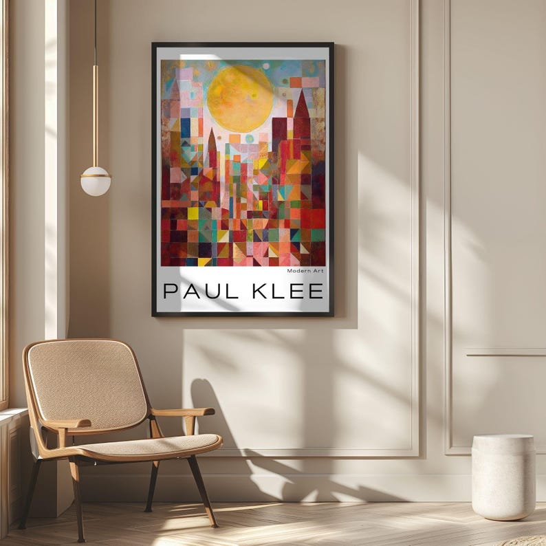 Peut inclure: Une affiche encadr&eacute;e repr&eacute;sentant un paysage urbain abstrait color&eacute; avec un grand soleil jaune. L'affiche est intitul&eacute;e "PAUL KLEE" et "Modern Art". L'&oelig;uvre est expos&eacute;e sur un mur beige, avec une chaise et une suspension luminaire visibles.