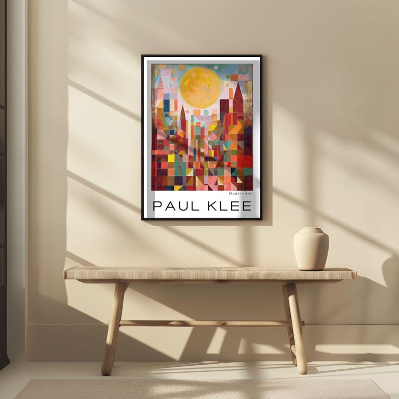 Peut inclure: Une affiche encadr&eacute;e repr&eacute;sentant un paysage urbain abstrait color&eacute; avec un grand soleil jaune. L'&oelig;uvre, de Paul Klee, pr&eacute;sente des formes g&eacute;om&eacute;triques et des teintes vives de rouge, de bleu et de jaune. L'affiche est affich&eacute;e au-dessus d'un banc en bois.