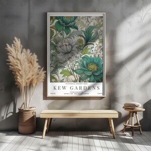 K&ouml;nnte beinhalten: Gerahmter Kunstdruck mit floralem Design in Gr&uuml;n-, Wei&szlig;- und Graut&ouml;nen. Der Druck tr&auml;gt die Aufschrift "Kew Gardens" und wird an einer grauen Wand gezeigt. Eine Holzbank und ein Hocker befinden sich vor der Wand.