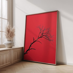 May include: A rectangular wall art print featuring a stark black silhouette of a leafless tree branch extending diagonally across a solid, vibrant red background, all encased within a thin, natural-toned wooden frame.