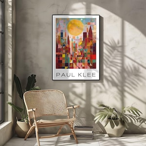 Peut inclure: Une affiche encadr&eacute;e repr&eacute;sentant une ville abstraite color&eacute;e avec un grand soleil jaune. L'affiche porte le nom "PAUL KLEE" en blanc en bas. L'&oelig;uvre est affich&eacute;e sur un mur gris, avec une chaise en bois et des plantes au premier plan.