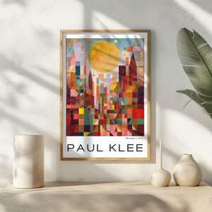 Peut inclure: Une affiche encadr&eacute;e d'un paysage urbain abstrait color&eacute; de Paul Klee. L'&oelig;uvre pr&eacute;sente un grand soleil jaune et des formes g&eacute;om&eacute;triques dans des tons de rouge, orange, bleu et vert. Le texte "PAUL KLEE" est affich&eacute; en bas.