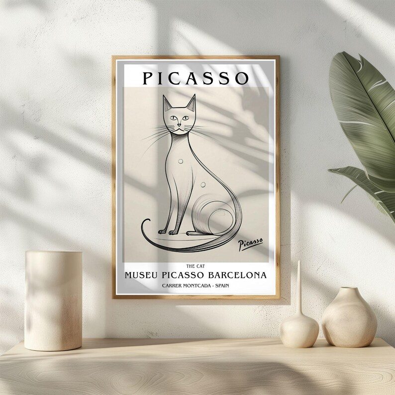 May include: Framed art print featuring a line drawing of a cat, with the name "PICASSO" at the top. The print includes text indicating the artwork is from the Museu Picasso Barcelona. The frame is a light brown color.