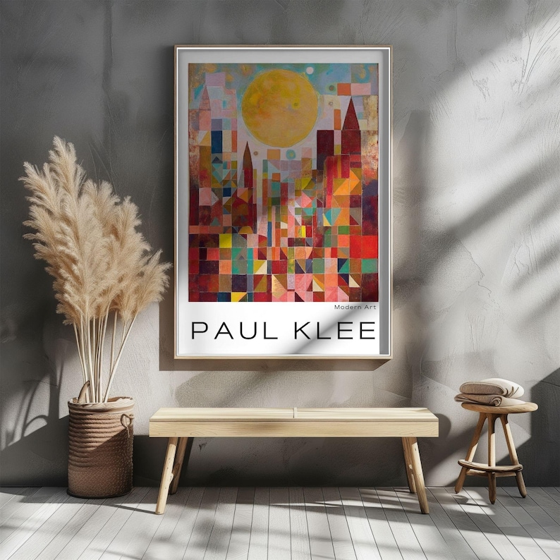 Peut inclure: Une affiche encadr&eacute;e repr&eacute;sentant un paysage urbain abstrait color&eacute; avec un grand soleil jaune. L'affiche est &eacute;tiquet&eacute;e "Modern Art" et "PAUL KLEE" en texte blanc. L'&oelig;uvre est affich&eacute;e sur un mur gris au-dessus d'un banc en bois.
