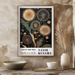 May include: A framed art print featuring a stylized floral design in shades of gold, orange, and green against a dark background. The print includes text that reads "JAPAN ART 1924 YAYOI KUSAMA" and Japanese characters.
