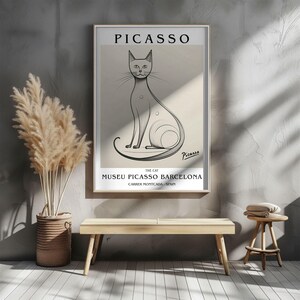 May include: A framed art print featuring a line drawing of a cat, with the name "Picasso" at the top. The print includes the text "The Cat" and "Museu Picasso Barcelona" with the address. The artwork is in a gold frame.