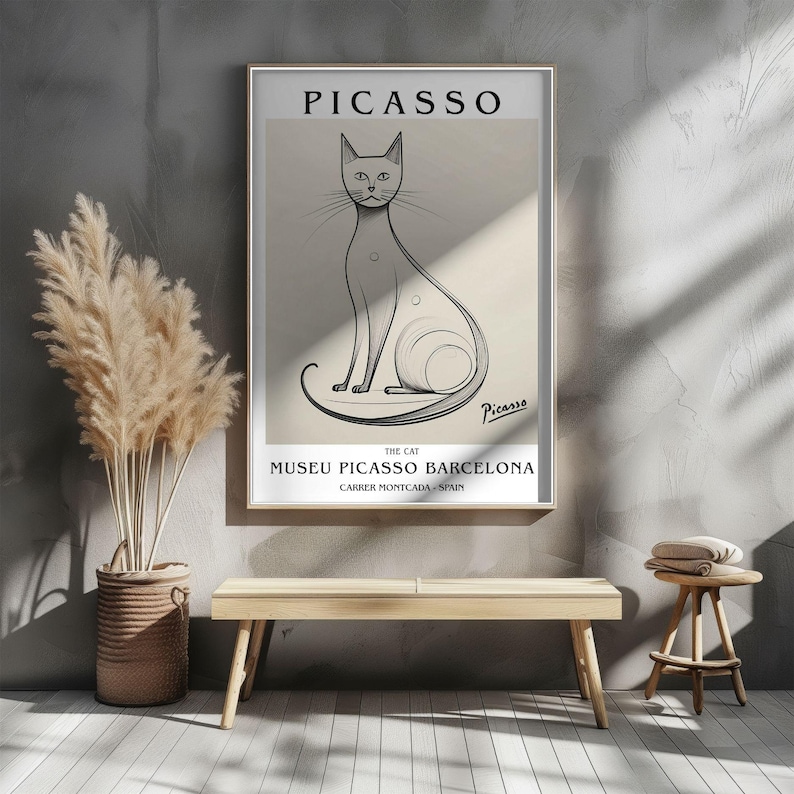 May include: A framed art print featuring a line drawing of a cat, with the name "Picasso" at the top. The print includes the text "The Cat" and "Museu Picasso Barcelona" with the address. The artwork is in a gold frame.