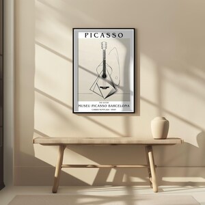 Puede incluir: Un cuadro enmarcado con una ilustraci&oacute;n en blanco y negro de una guitarra. La impresi&oacute;n incluye la palabra "PICASSO" en la parte superior y "MUSEU PICASSO BARCELONA" en la inferior. La obra de arte se exhibe sobre un banco de madera.