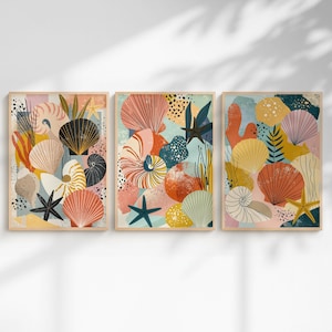 May include: Set of three framed art prints featuring colorful abstract illustrations of seashells, starfish, and coral. The artwork uses a palette of coral, teal, yellow, and black against a light background. The prints are in wooden frames.