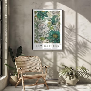 K&ouml;nnte beinhalten: Ein gerahmter botanischer Druck mit einem floralen Design in T&uuml;rkis und Wei&szlig;. Der Druck tr&auml;gt die Aufschrift "KEW GARDENS" und weitere Details. Der Druck wird an einer neutralen Wand mit einem Korbstuhl und Pflanzen im Vordergrund gezeigt.