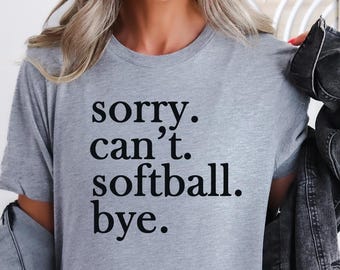 May include: A light grey t-shirt with the text "sorry. can't. softball. bye." in black. The person is wearing a black denim jacket. A cactus is visible in the background.