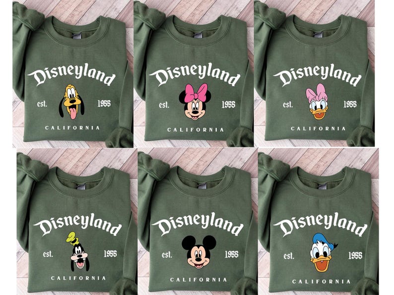 Puede incluir: Sudaderas verde oliva con la palabra "Disneyland" en escritura blanca, con varios rostros de personajes de Disney. Las sudaderas tambi&eacute;n muestran "est. 1955" y "CALIFORNIA" en texto blanco. Los personajes incluyen a Goofy, Minnie Mouse y Donald Duck.