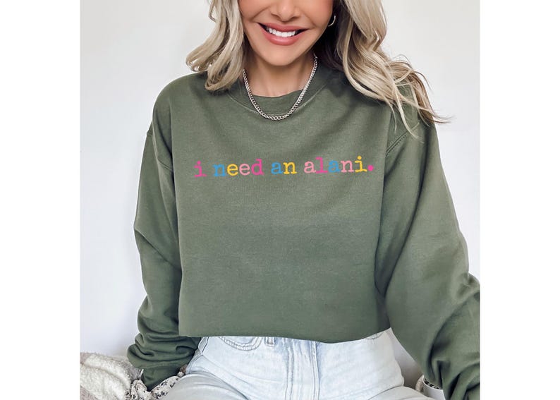 Op de afbeelding: Olijfgroene sweatshirt met de geborduurde tekst "I need an all nighter" in kleurrijke letters. De sweatshirt heeft een ronde hals en lijkt gemaakt van een zacht materiaal. De stijl is casual en comfortabel.