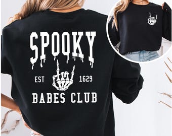 May include: Black sweatshirt featuring the text "SPOOKY BABES CLUB" in white, with a skeleton hand graphic. The back of the sweatshirt has the word "SPOOKY" in large, dripping letters. The front has a smaller skeleton hand graphic.