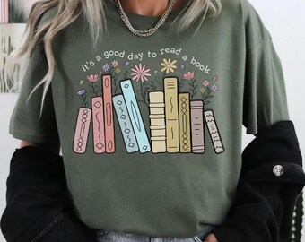 May include: An olive green t-shirt with the phrase "it's a good day to read a book". The design shows a row of colourful books with flowers. The books are in shades of pink, blue, yellow, and orange.