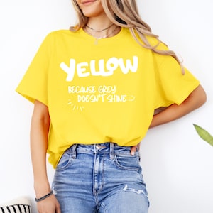 Könnte beinhalten: Ein gelbes T-Shirt mit dem Text "YELLOW because GREY doesn't shine" in Weiß. Das Shirt hat einen Rundhalsausschnitt und kurze Ärmel.