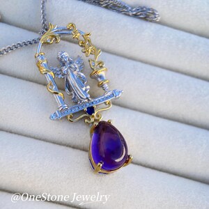 May include: A silver and gold pendant necklace with an angel figure in a decorative frame. A large, teardrop-shaped, deep purple gemstone hangs below. The necklace has a fine silver chain. The text "@OneStone Jewelry" is visible.