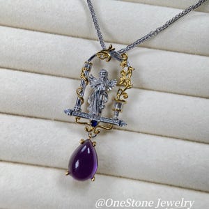May include: A silver and gold pendant necklace with an angel figure in an ornate frame. The pendant has a large, teardrop-shaped purple gemstone. The necklace is displayed on a white, textured surface. The text "@OneStone Jewelry" is visible.