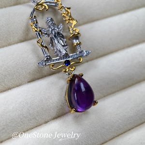 May include: A silver and gold pendant necklace with an angel figure in a decorative frame. The pendant has a large, teardrop-shaped, deep purple amethyst gemstone. The necklace is marked with the text "@OneStone Jewelry".