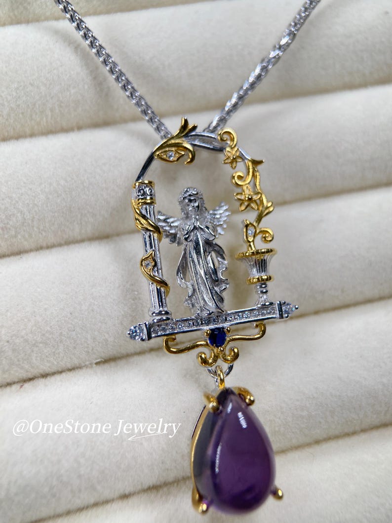 May include: A silver and gold pendant necklace with an angel design within a decorative frame. The pendant has a teardrop-shaped, deep purple gemstone. The necklace chain is silver. The text "@OneStone Jewelry" is visible.