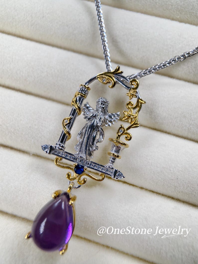 May include: A silver and gold pendant necklace with an angel design within a decorative frame. The pendant features a large, teardrop-shaped, purple gemstone. The necklace is on a silver chain. The text "@OneStone Jewelry" is visible.