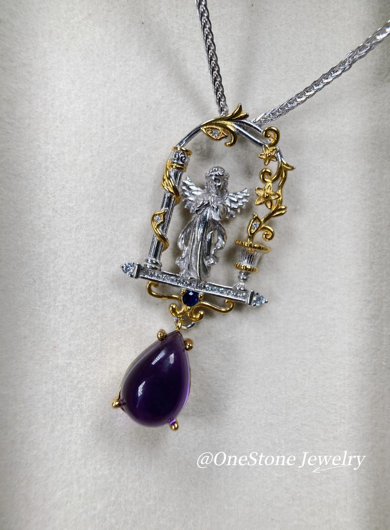 May include: Silver and gold-tone pendant necklace featuring an angel figure within a decorative frame. The pendant includes a teardrop-shaped, deep purple amethyst gemstone. The necklace has a silver chain.
