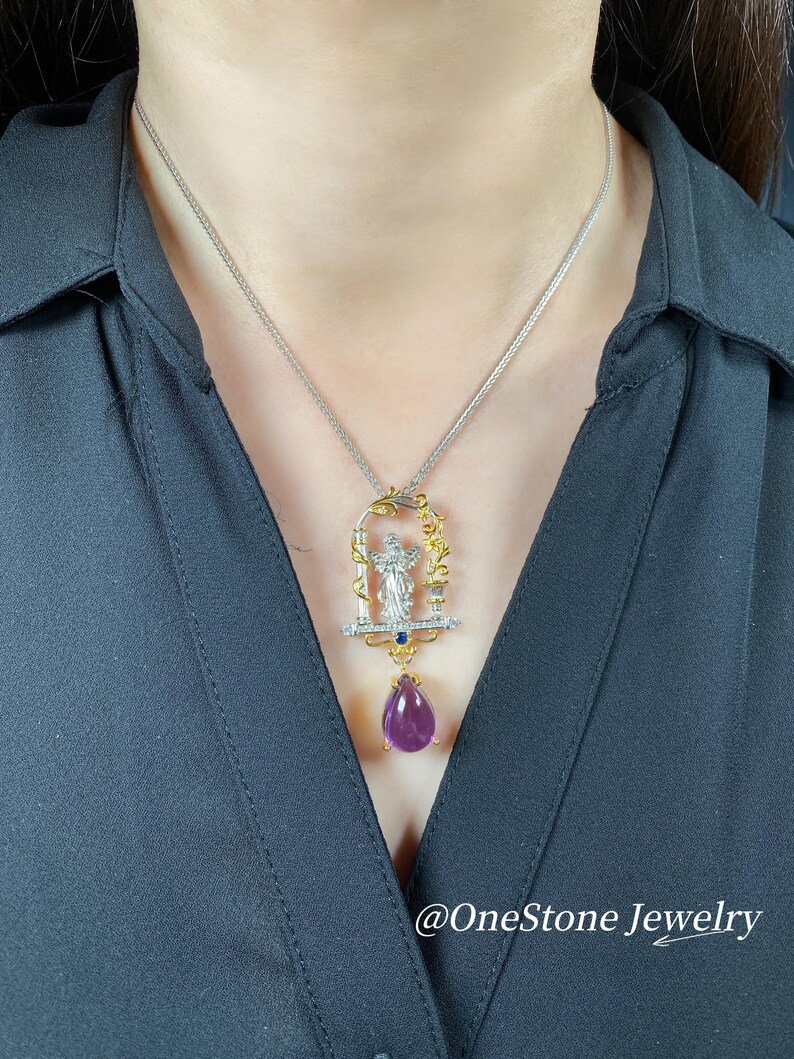 May include: A silver necklace with a gold pendant featuring a figure, clear stones, and a teardrop-shaped purple gemstone. The pendant hangs from a delicate silver chain. The text "@OneStone Jewelry" is at the bottom.