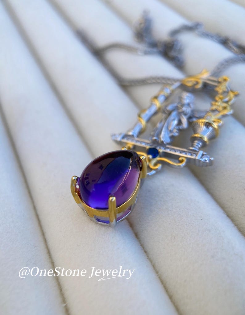 May include: A silver and gold pendant necklace with a large, teardrop-shaped purple gemstone. The pendant has a detailed design with a figure and is suspended from a delicate chain. The text "@OneStone Jewelry" is visible.