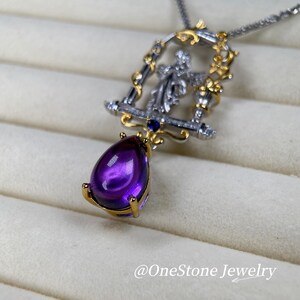 May include: A silver necklace with a pendant featuring a large, teardrop-shaped purple amethyst gemstone. The pendant has a gold-coloured frame with intricate detailing and a small figure. The necklace is displayed on a light-coloured surface. The text "@OneStone Jewelry" is visible.