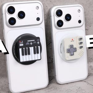 May include: Two white phone cases with attached accessories. One case features a black and white keyboard design, and the other has a gray game controller design. Both cases have a camera array at the top.