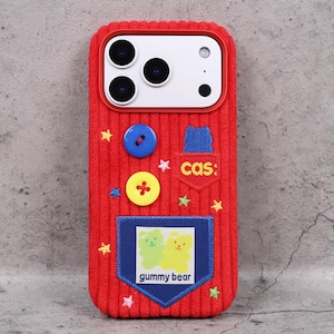 May include: Red corduroy phone case with a playful design. Features a blue and yellow button, a small pocket with the text "cas:" and a patch with two gummy bear illustrations. The case is decorated with embroidered stars.