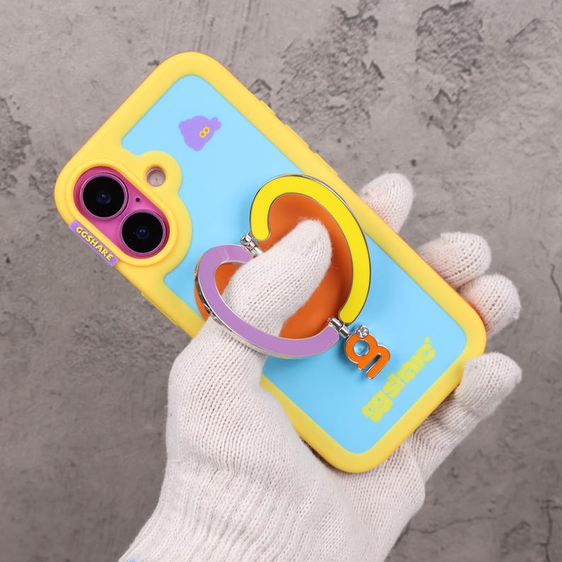 May include: A yellow and blue phone case with a heart-shaped ring holder. The case has a light blue background with a purple cloud graphic. The ring holder is purple, yellow, and orange. The text "GGSHARE" is visible.