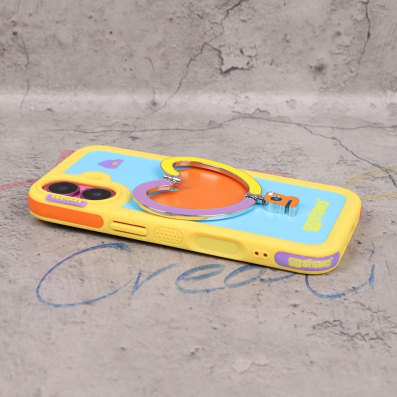 May include: A yellow and blue phone case with a heart-shaped design. The case has an orange and purple heart-shaped accent with a silver outline. The case has the word "GGshine" printed on the bottom. The phone case has a camera cutout.