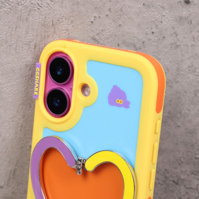 May include: A yellow, blue, and orange phone case with a heart-shaped stand. The case has a cartoon design and the text "GGSHARE" in purple. The phone case has a dual-camera design.