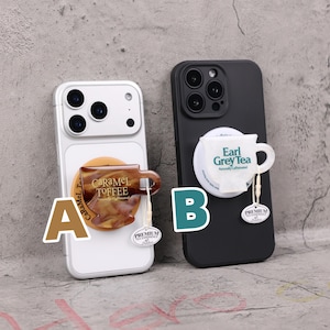 May include: Two phone cases, one white and one black, each with a unique tea-themed design. The white case features a caramel toffee cup, while the black case showcases an Earl Grey Tea bag. Both designs include a "Premium Tea Essence" tag.