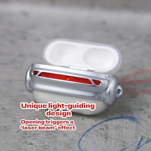 May include: A white and silver case for earbuds with a red light-guiding design. The text on the case reads "Unique light-guiding design" and "Opening triggers a 'laser beam' effect."