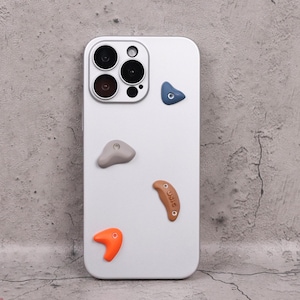 May include: A white phone case with a camera module and colorful climbing holds. The case has a gray, blue, orange, and brown climbing hold design. The brown hold has the text "USIS" on it.
