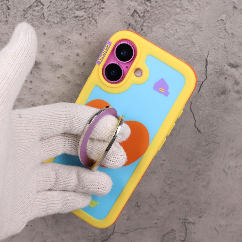 May include: A yellow, blue, and orange phone case with a heart design and a purple and silver phone ring. The case has the text "GGSHARE" on the side.