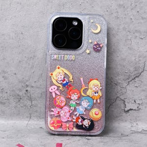 Puede incluir: Una funda transparente para teléfono con un fondo rosa brillante y una variedad de personajes de dibujos animados coloridos del anime Sailor Moon. La funda tiene el texto "SWEET DODO" impreso en la parte posterior.