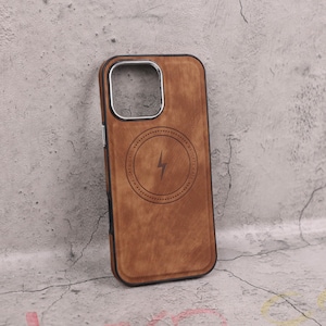Könnte beinhalten: Braune Handyhülle aus Holz mit schwarzem Rand. Die Hülle hat einen silbernen Kameraausschnitt und ein kreisförmiges Design mit einem Blitzsymbol. Die Worte "MAGSAFE CASE" sind um den Kreis herum aufgedruckt.