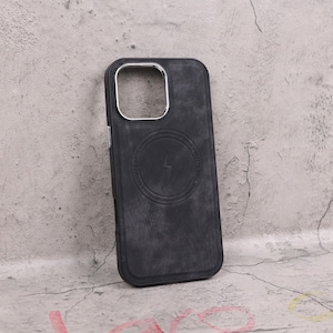 Könnte beinhalten: Eine dunkelgraue Handyhülle mit strukturierter Oberfläche. Die Hülle hat einen silberfarbenen Kameraring und ein kreisförmiges Design mit einem Blitzsymbol. Die Hülle schützt das Telefon und trägt die Aufschrift "NOVAFE CASE".