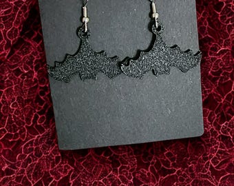 May include: A pair of black glitter bat earrings on a black card. The earrings have silver hooks.