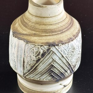 May include: A small, brown and white ceramic vase with a geometric pattern. The vase has a wide base and a narrow neck.