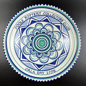 May include: A white ceramic plate with a blue and green geometric design. The plate has the text "Poole Pottery Collectors Club Gala Day 1996" around the edge.