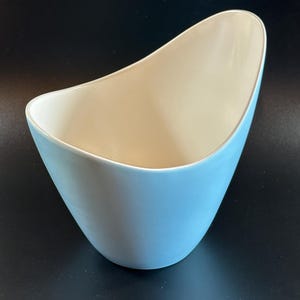 May include: A light blue ceramic vase with a unique, asymmetrical shape. The vase has a smooth, glossy finish.