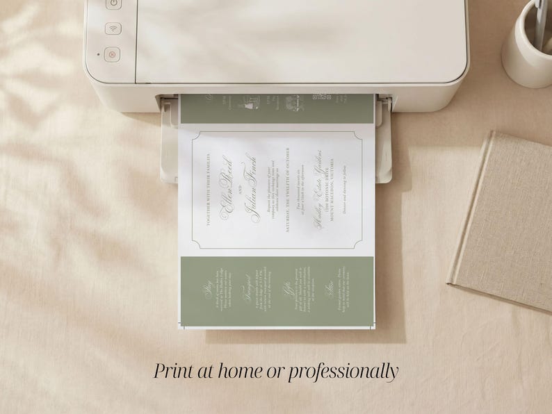 May include: A white home printer outputting a wedding invitation card featuring sage green accents and white text. The invitation displays the names Ellen Reed and Julian Finch, along with event details, framed by a thin border on a white background.
