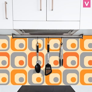 May include: A retro-style kitchen backsplash with a repeating pattern of orange, gray, and cream-colored squares. A black utensil rack holds a spoon, spatula, and tongs. White cabinets are above.