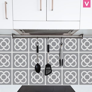 Puede incluir: Escena de cocina con armarios blancos, un salpicadero con estampado gris y blanco y un estante metálico para utensilios. Cuelgan del estante una cuchara, una espátula y unas pinzas negras. El salpicadero presenta un diseño floral repetitivo.